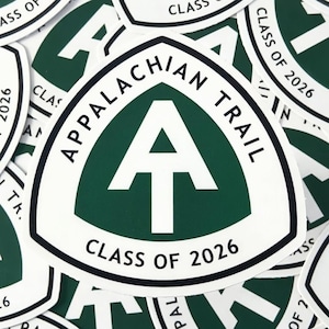 May include: White and green Appalachian Trail stickers. The stickers are triangular with the words "APPALACHIAN TRAIL" and "CLASS OF 2026" in black text. The center features a white arrow on a green background.