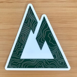May include: A white sticker with a green mountain range design. The mountains are outlined in white and have a topographic map pattern.