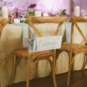 May include: A wooden chair with a light blue ribbon tied around the back. A white card with the word "Matchmaker" written in black calligraphy is attached to the ribbon.