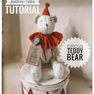 May include: A white teddy bear wearing a red ruffled collar and a matching hat, sitting atop a round box with red and white geometric designs. The image includes text that reads "PDF sewing pattern + video TUTORIAL" and "CIRCUS TEDDY BEAR".
