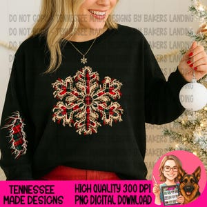 Puede incluir: Una sudadera negra de manga larga con un gran gráfico de copo de nieve central con un patrón de cuadros rojo, verde y blanco. Un diseño de copo de nieve a cuadros a juego también es visible en la manga inferior. La prenda tiene cuello redondo.