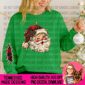 Puede incluir: Una sudadera verde brillante de manga larga con un gráfico de un Santa Claus guiñando un ojo y usando un gorro de cuadros rojos y negros. La manga izquierda muestra un parche a juego de cuadros rojos y negros con bordes deshilachados.