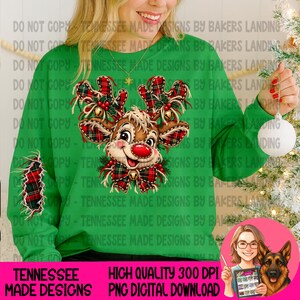 May include: A bright green long-sleeve sweatshirt featuring a central graphic of a reindeer with plaid antlers and a matching plaid bow tie. The reindeer has a red nose and holly berry accents. A plaid patch is visible on the left sleeve.
