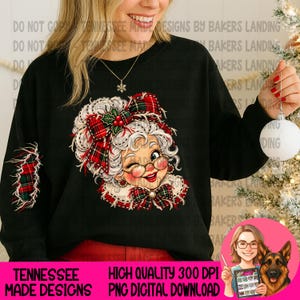 Puede incluir: Una sudadera negra de manga larga con un gráfico de la señora Claus guiñando un ojo, con pelo blanco, gafas redondas y un lazo de cuadros rojos y verdes. La manga tiene un parche de cuadros a juego y detalles de acebo.