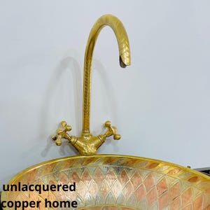 Puede incluir: Un lavabo de cobre sin laquear con un diseño decorativo y estampado. El lavabo tiene una forma ovalada y cuenta con un grifo a juego en tono dorado con una sola manija.