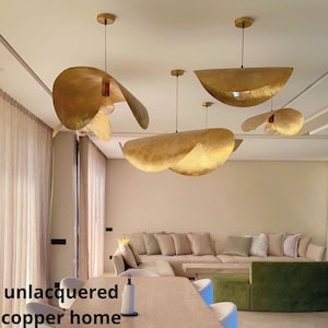 Puede incluir: Un salón moderno con un gran sofá seccional y un conjunto de cinco lámparas colgantes de cobre sin lacar únicas. Las lámparas tienen forma de grandes hojas superpuestas.