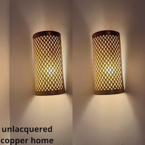 May include: Two unlacquered copper wall sconces with a geometric pattern. The sconces are lit and casting a warm glow.