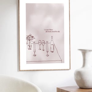 Könnte beinhalten: Gerahmter Kunstdruck mit einer minimalistischen Strichzeichnung einer Tischdekoration. Das Kunstwerk umfasst eine Weinflasche, Gläser und ein Blumengesteck. Der Text lautet: „Ich habe es mit Freunden um den Tisch tanzen sehen.“