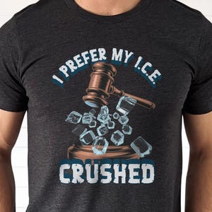 May include: Dark gray t-shirt with the text "I PREFER MY I.C.E. CRUSHED." A brown gavel is depicted above a collection of ice cubes. The design is in white and blue.