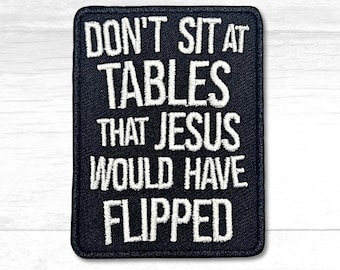 Könnte beinhalten: Ein rechteckiger schwarzer Aufnäher mit weiß gesticktem Text. Der Text lautet: "DON'T SIT AT TABLES THAT JESUS WOULD HAVE FLIPPED."