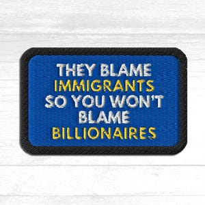 Könnte beinhalten: Gestickter Aufnäher mit blauem Hintergrund und schwarzem Rand. Der Text "THEY BLAME IMMIGRANTS SO YOU WON'T BLAME BILLIONAIRES" ist in weißer und gelber Schrift gestickt.
