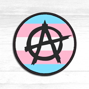 May include: Round patch featuring the anarchy symbol, a capital "A" within a circle, in black. The background displays the transgender pride flag colors: light blue, pink, and white stripes. The patch has a black border.