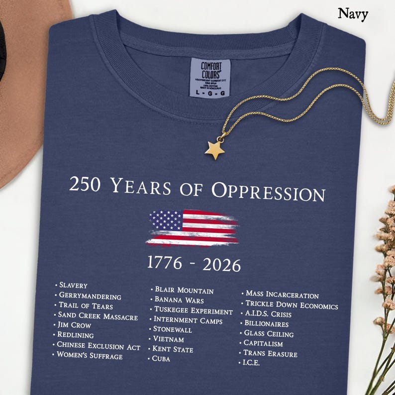 Pode incluir: Uma t-shirt azul-marinho de manga curta com o texto branco 250 YEARS OF OPPRESSION 1776 - 2026, um gr&aacute;fico da bandeira americana e uma lista de eventos hist&oacute;ricos incluindo Slavery, Jim Crow e Mass Incarceration em fonte branca.
