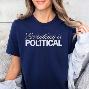 May include: Navy blue t-shirt with the white text "Everything is POLITICAL". The shirt has a crew neck and short sleeves. The text is in a stylized font.