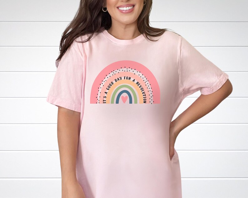 May include: A pink t-shirt featuring a rainbow graphic and the text "It's a good day for a revolution".