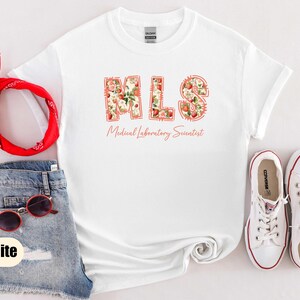 Puede incluir: Camiseta blanca con las letras "MLS" en un dise&ntilde;o floral, con las palabras "Medical Laboratory Scientist" debajo. La imagen tambi&eacute;n incluye pantalones cortos de mezclilla, gafas de sol rojas, una bandana roja y zapatillas blancas.