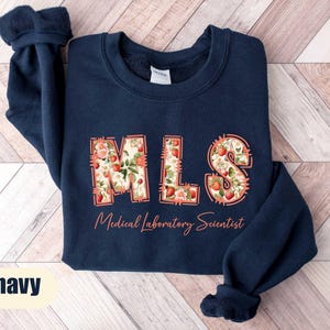 Puede incluir: Sudadera azul marino con las letras "MLS" en un dise&ntilde;o floral, con las palabras "Medical Laboratory Scientist" en cursiva. La sudadera es de color azul marino liso.