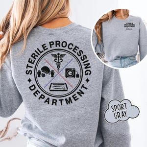 May include: A sport gray sweatshirt featuring a black graphic on the back with the text STERILE PROCESSING DEPARTMENT surrounding icons of a caduceus, surgical cap, gloves, autoclave, and tray. The front chest displays the same text and a name.