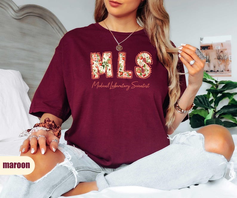 Puede incluir: Camiseta granate con el texto "MLS Medical Laboratory Scientist" en un dise&ntilde;o floral. La camiseta es de color granate liso y tiene cuello redondo.