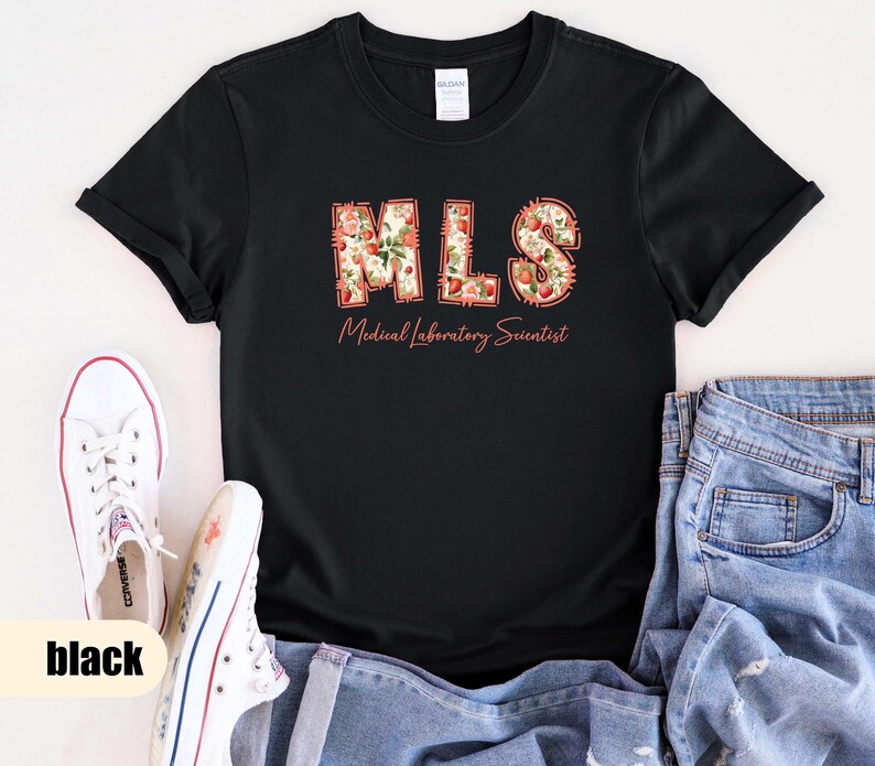Puede incluir: Camiseta negra con las letras "MLS" en un dise&ntilde;o floral, con las palabras "Medical Laboratory Scientist" debajo. Zapatillas blancas y vaqueros azules tambi&eacute;n est&aacute;n en la imagen.