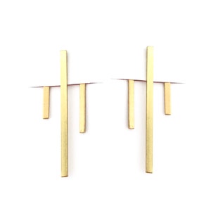 May include: A pair of gold geometric earrings with a long vertical bar and three shorter horizontal bars.