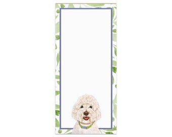 May include: White notepad with a green and white floral border. A white dog with a green collar is peeking out from the bottom of the notepad.