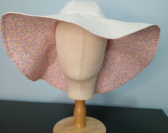May include: A white sun hat with a wide brim, displayed on a mannequin head. The underside of the brim features a floral pattern in pink, yellow, and blue. The hat is made of a sturdy fabric and is designed for sun protection.