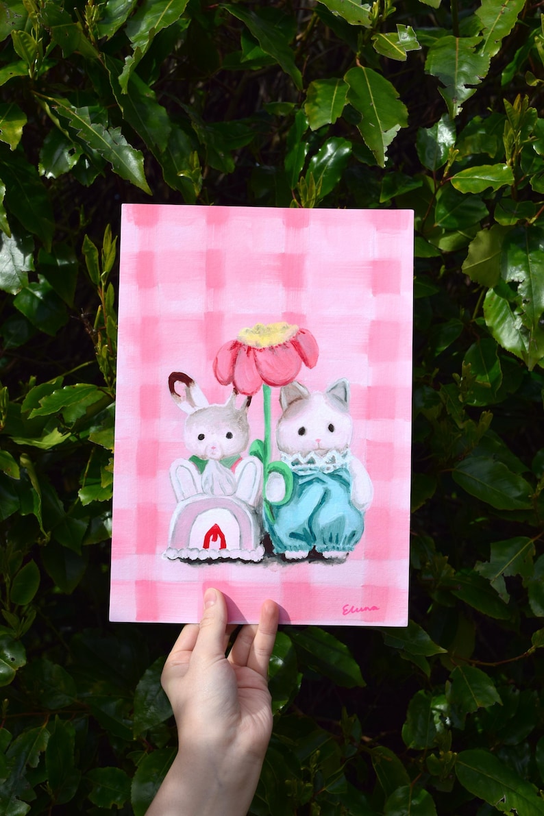 Peut inclure: Peinture fantaisiste repr&eacute;sentant un lapin et un chat anthropomorphes pr&egrave;s d'une grande fleur rose. Le fond est un motif &agrave; carreaux roses. Le lapin porte une tenue blanche avec un arc-en-ciel et une flamme rouge. Le chat porte une salopette bleue.