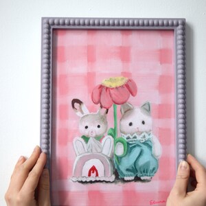 Peut inclure: Peinture encadr&eacute;e repr&eacute;sentant deux personnages de dessins anim&eacute;s, un lapin et un chat, pr&egrave;s d'une grande fleur rose. Le fond est un motif &agrave; carreaux roses et blancs. Le cadre est de couleur violet clair.