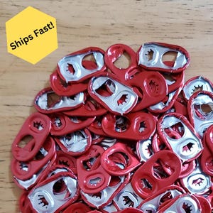 Puede incluir: Un montón de pestañas rojas y plateadas de latas de refresco. Las pestañas son de color rojo metálico con tiradores plateados. La imagen incluye un hexágono amarillo con el texto "Ships Fast!"