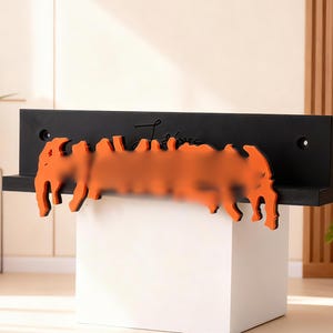 Peut inclure: Une étagère noire avec un élément décoratif orange. L'élément orange a une forme stylisée et le mot "Love" est écrit sur l'étagère. L'étagère est montée sur un cube blanc.