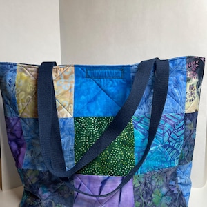 May include: A blue and green patchwork tote bag with navy blue straps. The bag is made of quilted fabric with a variety of floral and geometric patterns.