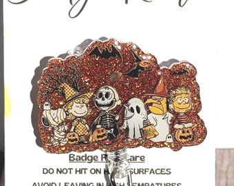 May include: A Halloween-themed badge reel featuring a glittery design with cartoon characters in costumes. The reel has a retractable cord and a snap-on clip. The text "Badge Reel" is at the top.
