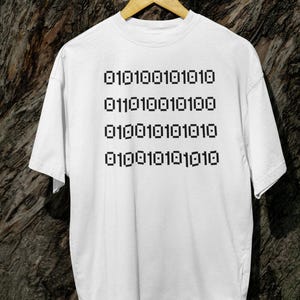 Peut inclure: T-shirt blanc avec un motif noir de code binaire répété : 0101000101010 01101100010100 0100010101010 0100010101010