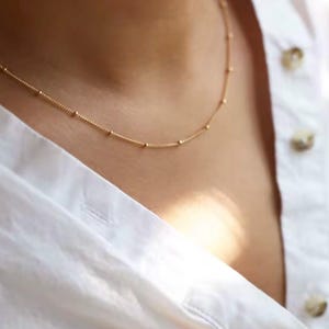 May include: A delicate gold chain necklace with small round beads.