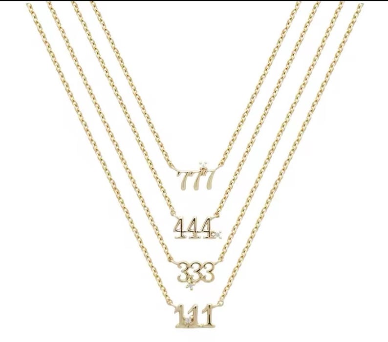 May include: A gold layered necklace with four pendants featuring the numbers 111, 333, 444, and 777, each with a small diamond accent.