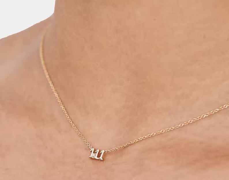 May include: A gold chain necklace with a small pendant featuring the number 111 with a single diamond in the center.