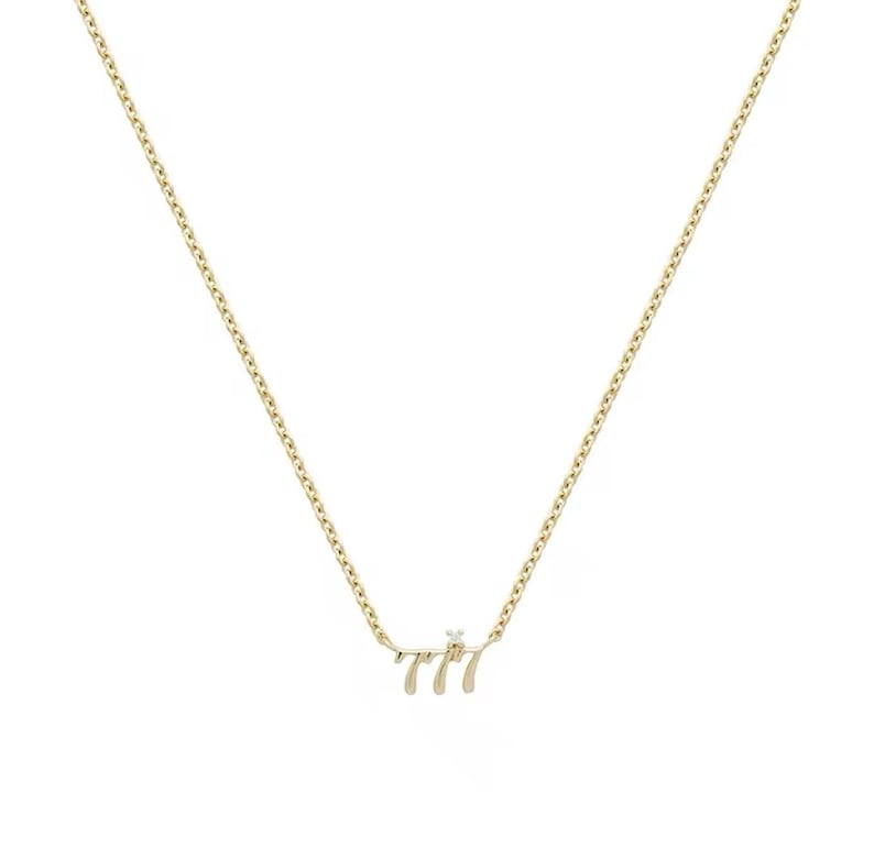 May include: A gold chain necklace with a pendant that says "777" with a small diamond in the center.