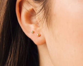 Puede incluir: Primer plano de la oreja de una persona con dos pequeños pendientes de bola de oro.