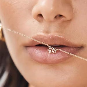 May include: A gold chain necklace with a small, delicate flower charm. The chain is thin and delicate, and the flower charm is made of gold and has a small diamond in the center.