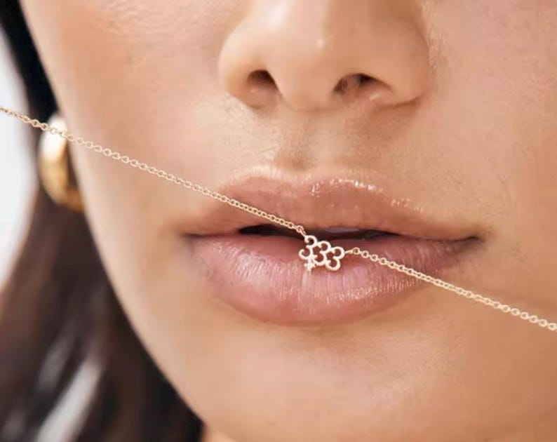 May include: A gold chain necklace with a small, delicate flower charm. The chain is thin and delicate, and the flower charm is made of gold and has a small diamond in the center.