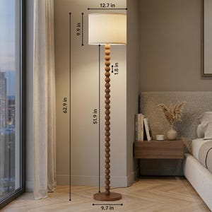 May include: A floor lamp with a cylindrical beige fabric shade and a tall, slender stem composed of stacked wooden spheres. The lamp stands 62.9 inches tall, with a 12.7-inch shade diameter, a 9.7-inch base diameter, and 1.8-inch wide spheres.