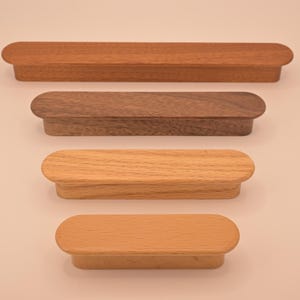 May include: Four wooden drawer pulls in different wood finishes. The pulls are oval shaped and have a smooth, polished finish. The pulls are arranged in a vertical stack from top to bottom: brown, dark brown, light brown, and beige.