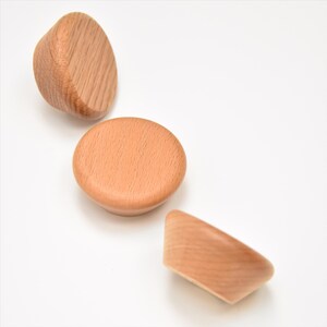May include: Three wooden knobs in different shapes. The knobs are light brown and have a smooth finish.