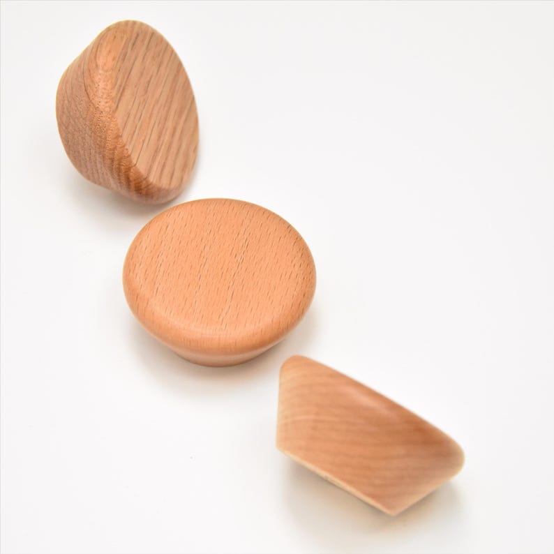 May include: Three wooden knobs in different shapes. The knobs are light brown and have a smooth finish.
