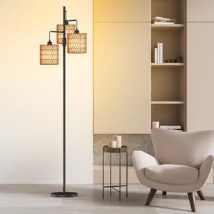 May include: A black floor lamp with three light fixtures. Each fixture has a woven, tan lampshade. The lamp is in a modern living room setting with a neutral color palette, including a beige armchair and a small side table.