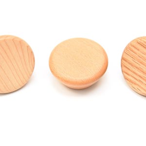 May include: Three wooden knobs with a light brown finish. The knobs have a round shape and a slightly raised edge.