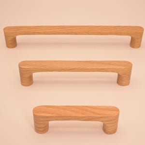 Puede incluir: Tres tiradores de armario de madera en diferentes tamaños. Los tiradores son de madera marrón claro y tienen un diseño simple y redondeado.