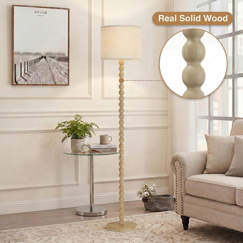 May include: A floor lamp with a tall, slender stand composed of stacked light-colored wooden spheres. The lamp features a cylindrical off-white fabric shade. A circular inset highlights the texture of the real solid wood construction.