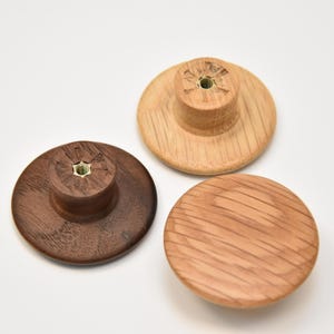 May include: Three wooden knobs in different wood types. The knobs are round and have a flat top. The knobs are all the same size.